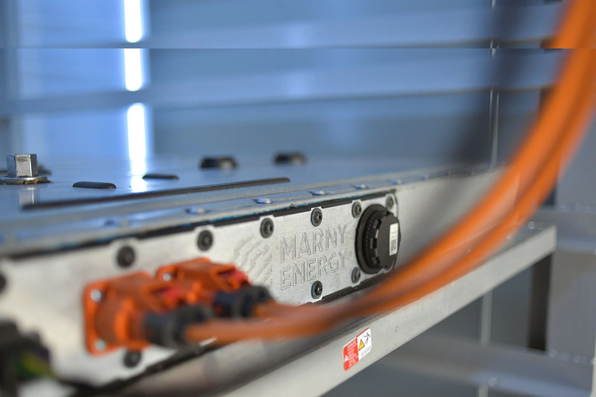 Close-up of a certified second-life EV battery module with the MARNY ENERGY logo embossed in metal and orange high-voltage cabling